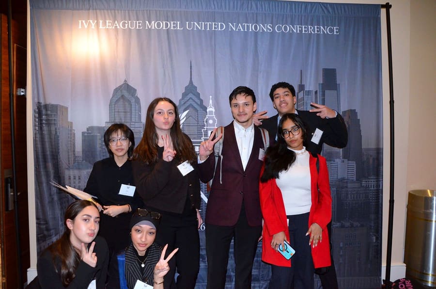 Delegates smiling and flashing peace signs in front of the conference banner